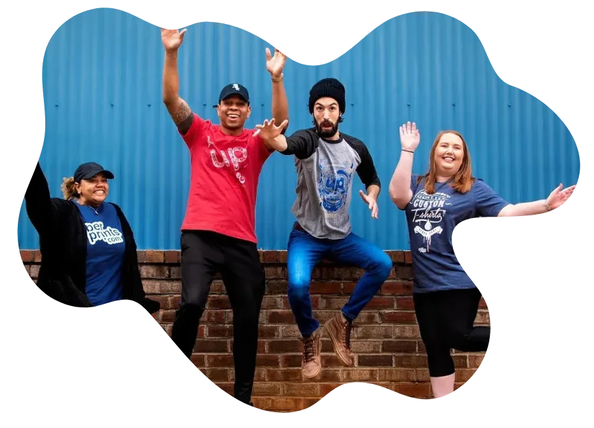 A diverse team of four smiling people in custom T-shirts jumping in front of a blue wall, showing energy and unity.